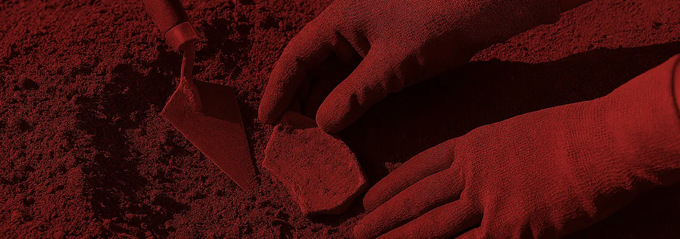 gloved hands handling a pottery shard with a trowel nearby