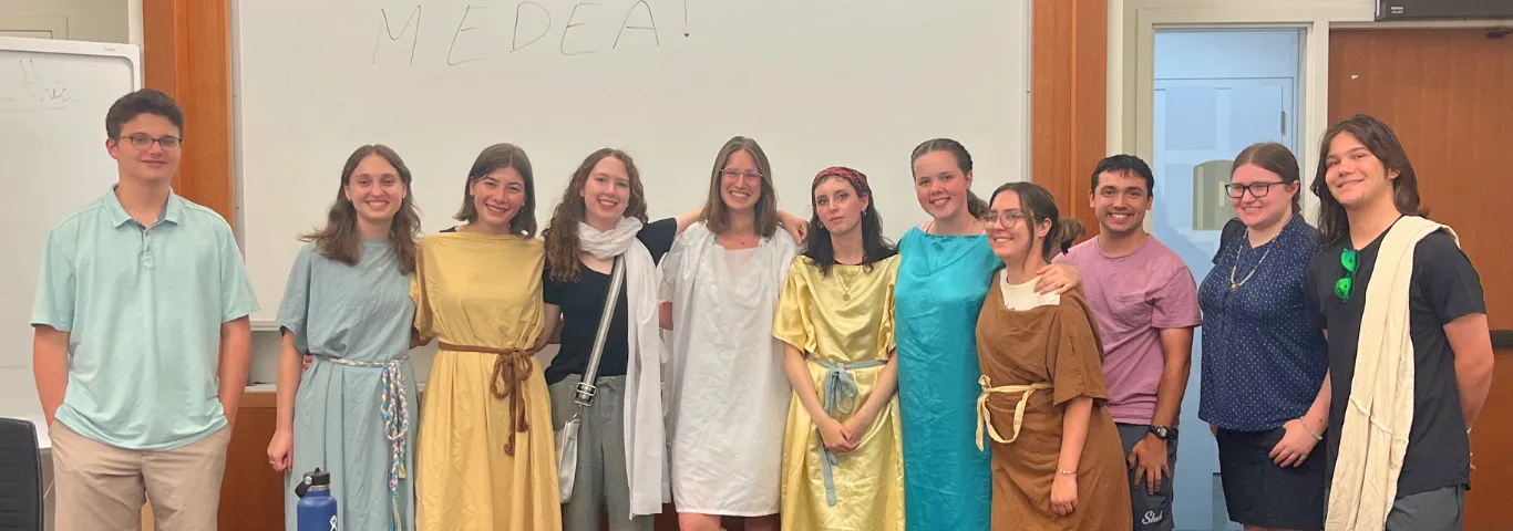 11 students lined up, some in costumes of greek tunics