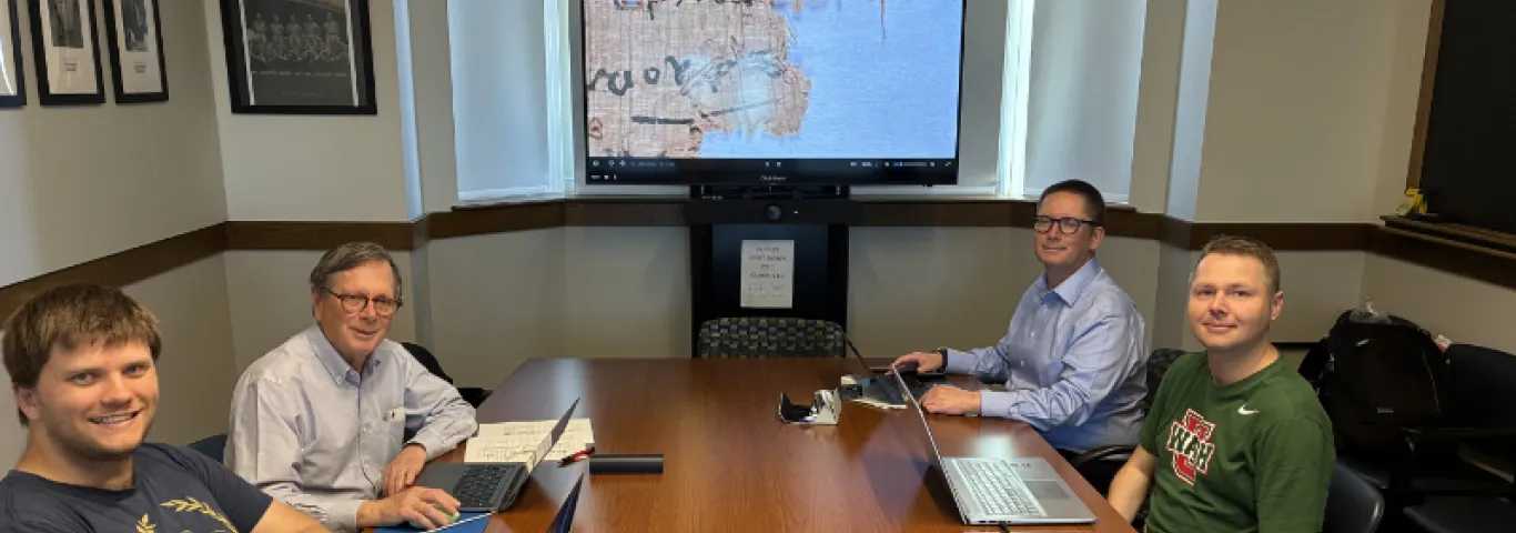 Editorial Team sitting at conference table with close up image of papyri on screen behind them