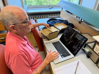 Moore at his laptop with hand in an index file and notepaper