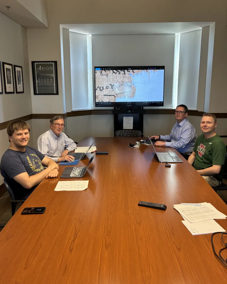 Editorial Team sitting at conference table with close up image of papyri on screen behind them