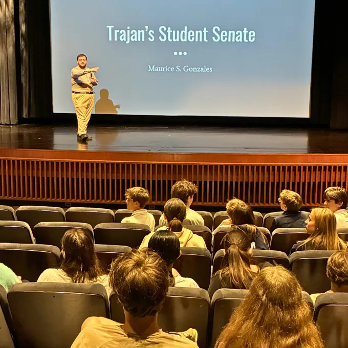 Gonzales in front of a screen "Trajan's Student Senate"